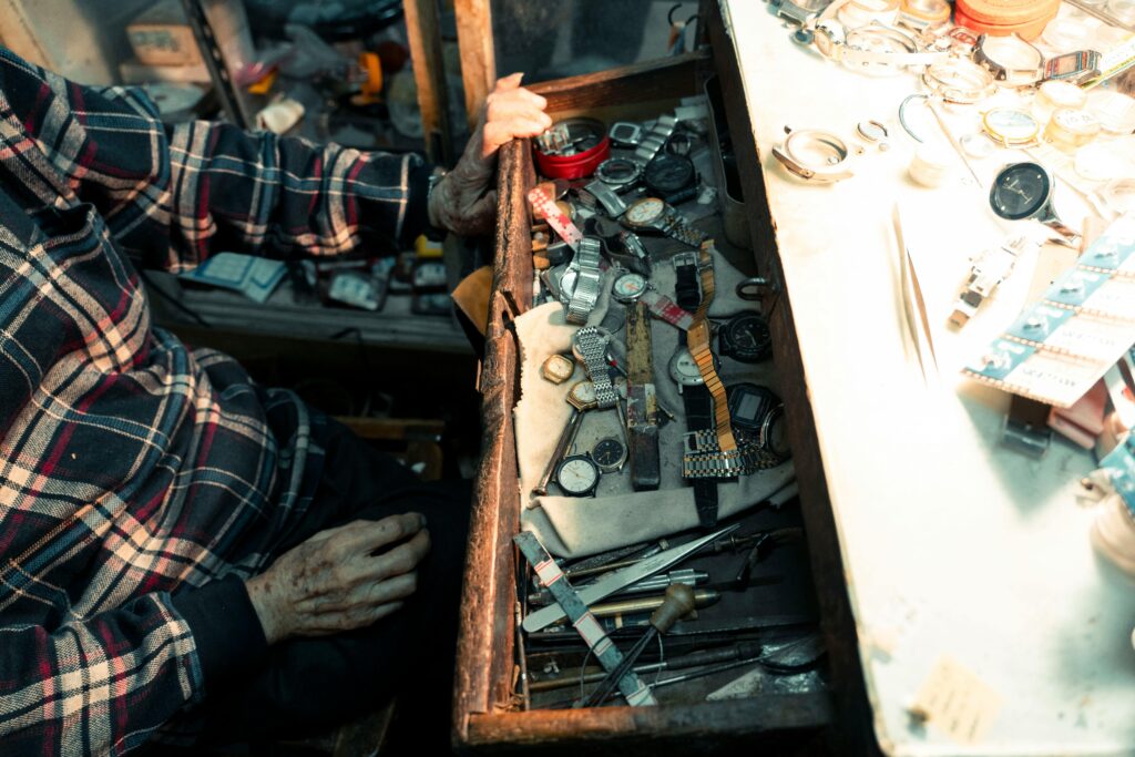 An artisan's hand at a workshop opens a drawer filled with watches, showcasing detailed repair tools.